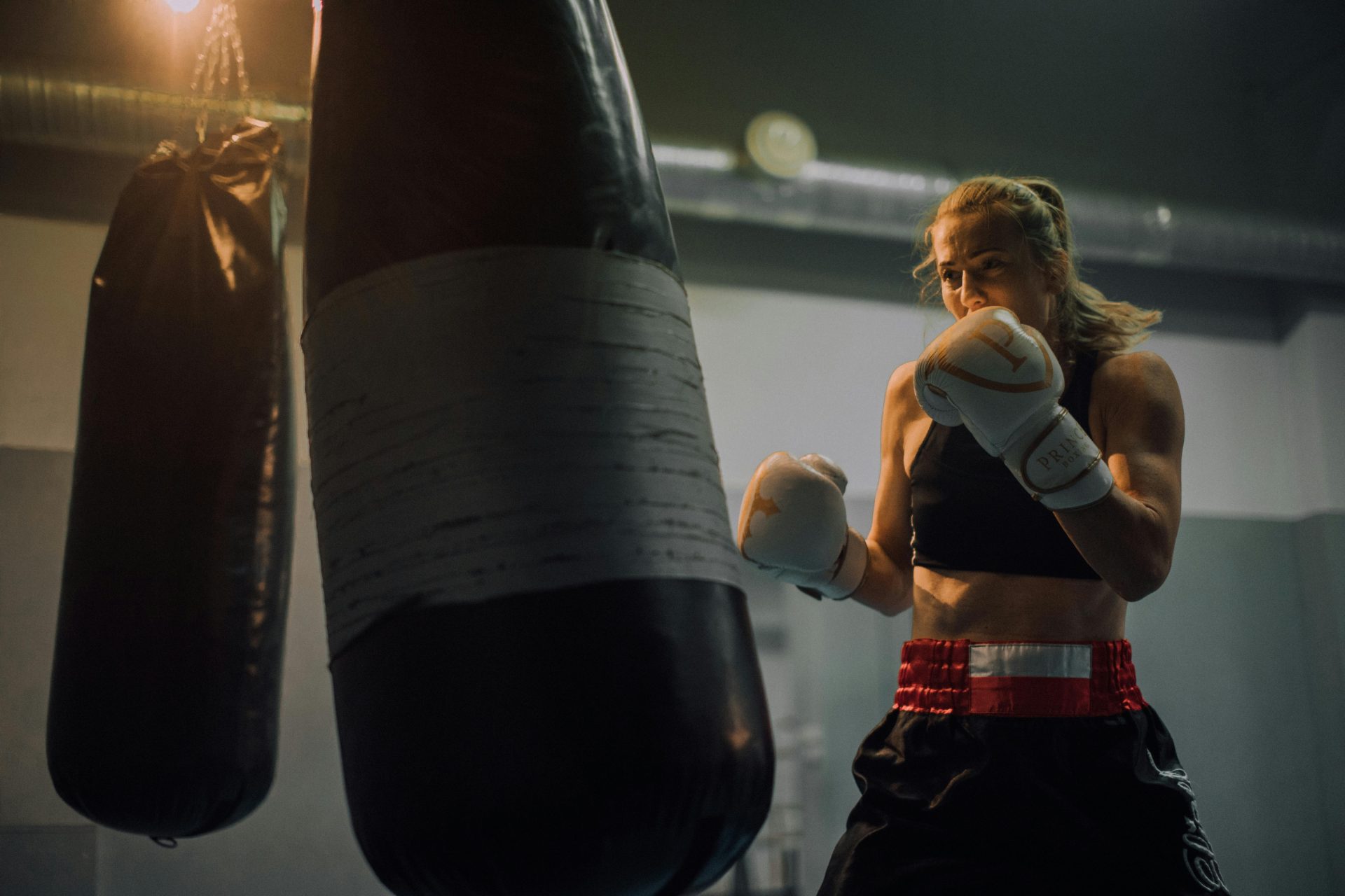 Una feroz boxeadora perfecciona sus habilidades en un gimnasio, lanzando poderosos golpes a un saco pesado.