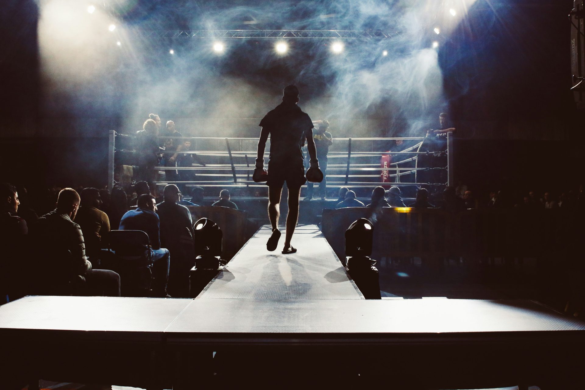 Hombre de pie y caminando hacia el ring de boxeo rodeado de gente.
